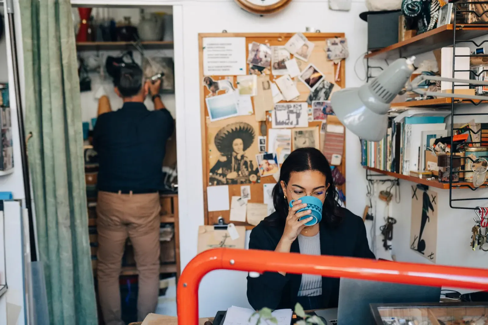 Kvinna dricker kaffe på rörigt, kreativt kontor